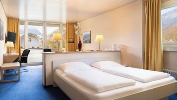 Ein Hotelzimmer mit Bett, Schreibtisch, Stuhl, Lampen und einem fenster mit Vorhängen.