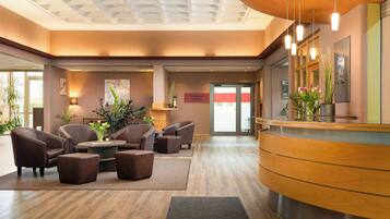 A hotel lobby with a reception desk, seating area, and a sign indicating a restaurant.