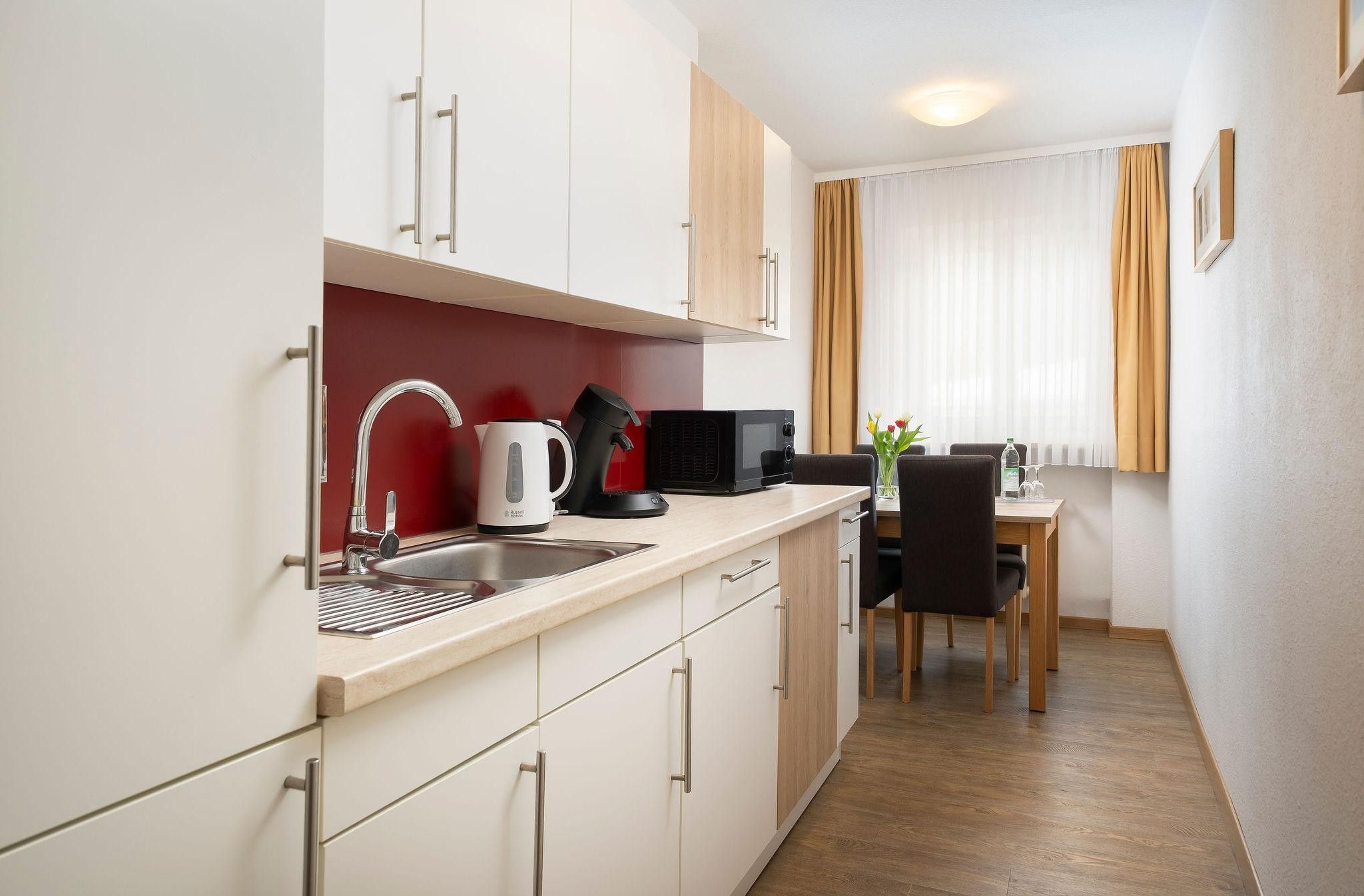 A compact kitchen with a sink, kettle, and microwave, leading to a dining area with a table and chairs.