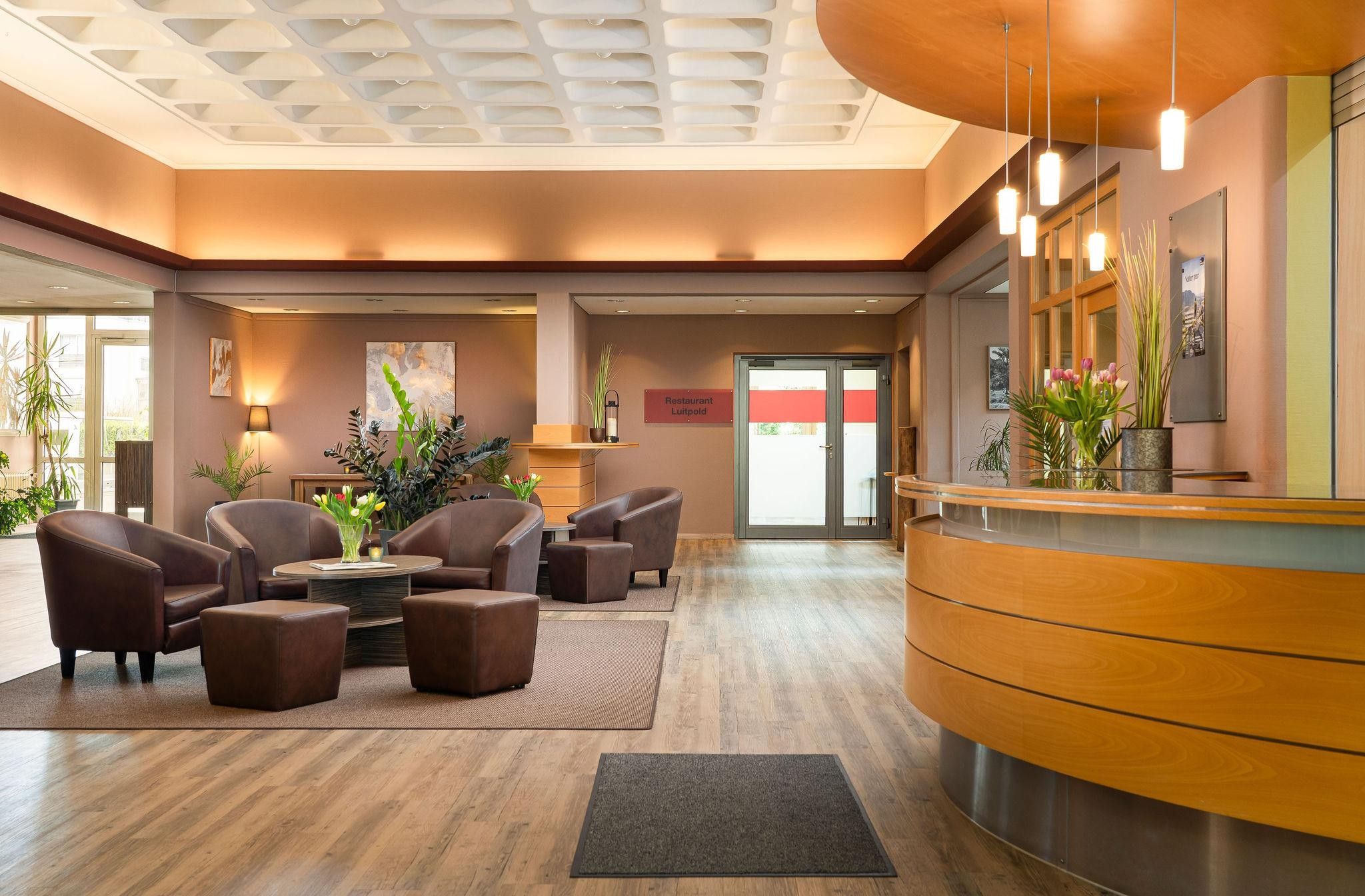 Eine Hotelhalle mit Ledersesseln, einem Empfangstresen und einer großen Pflanze.