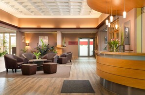A hotel lobby with leather armchairs, a reception desk, and a large plant. - Hotel Bayern Vital (Bad Reichenhall)