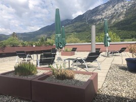 Terraza en la azotea con mobiliario exterior, sombrillas verdes y montañas al fondo.