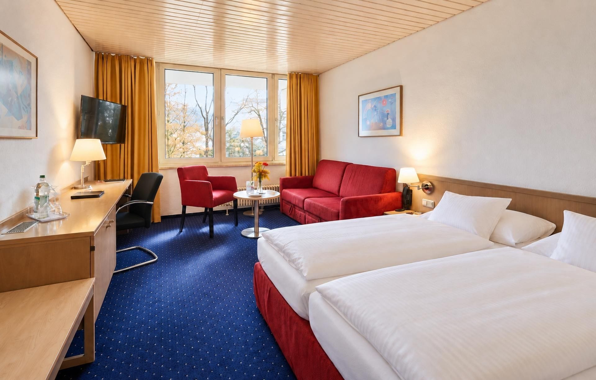 Ein Hotelzimmer mit Bett, Schreibtisch, Sessel, Sofa und Fernseher.