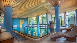 A modern indoor pool area with a wooden ceiling, blue walls, and a large window overlooking greenery. - Hotel Bayern Vital (Bad Reichenhall)