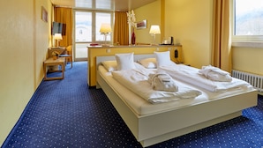 A hotel room with a large bed, two bedside lamps, a desk with a chair, a TV, and a window with curtains. - Hotel Bayern Vital (Bad Reichenhall)