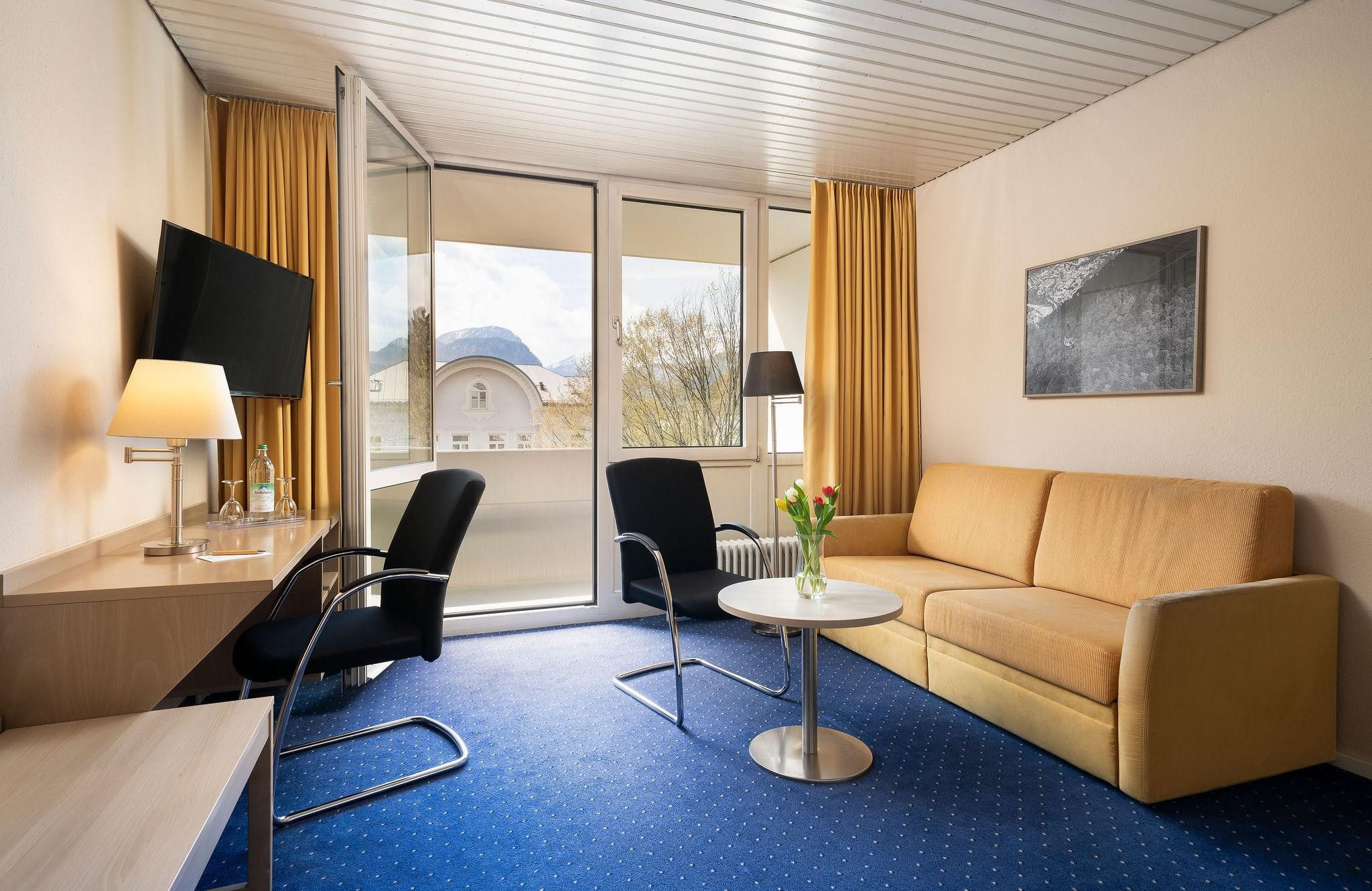 Une chambre d’hôtel avec un canapé, une petite table, une chaise, un téléviseur et une fenêtre avec des rideaux.