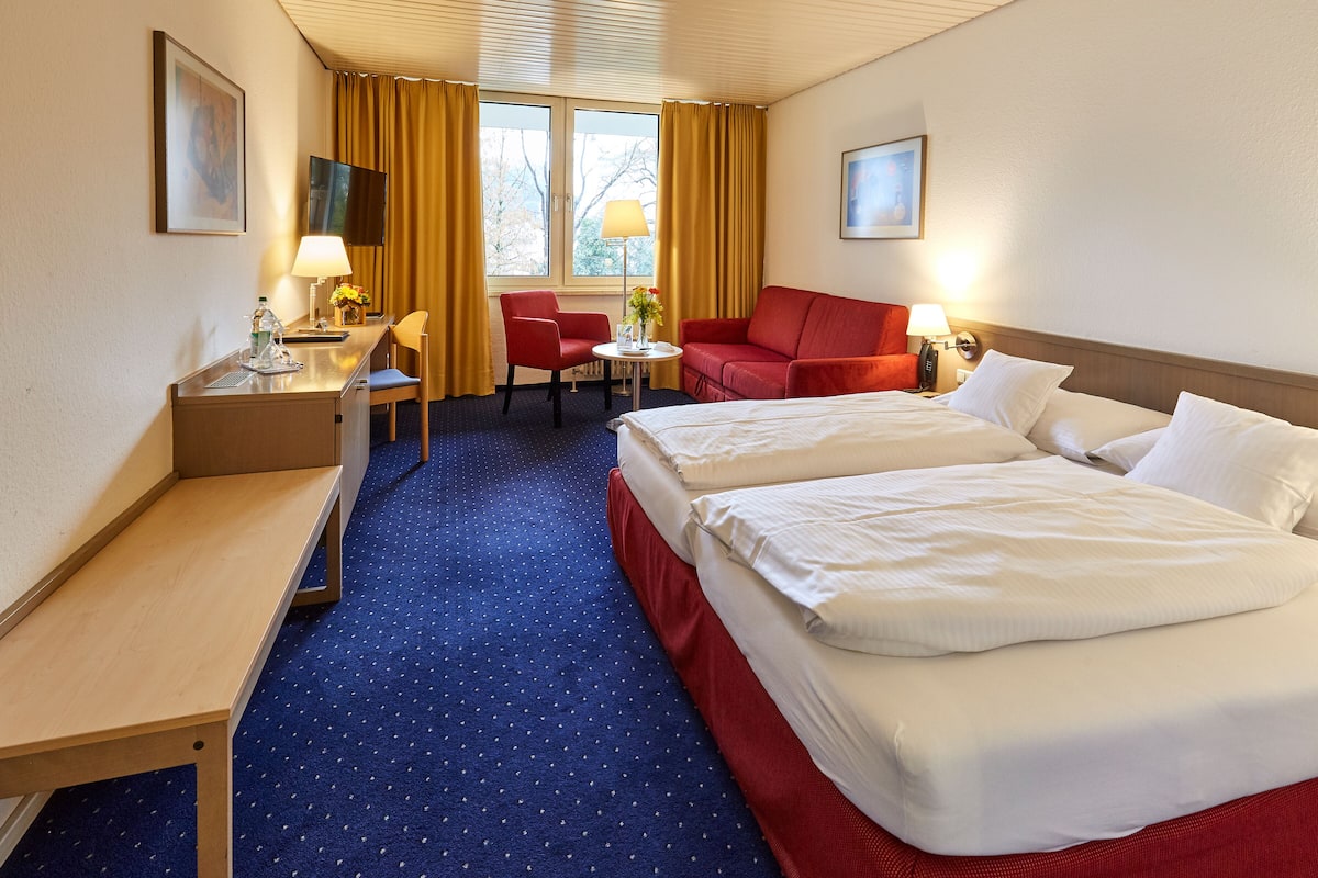 A hotel room with a bed, a desk, a chair, a sofa, and a TV.