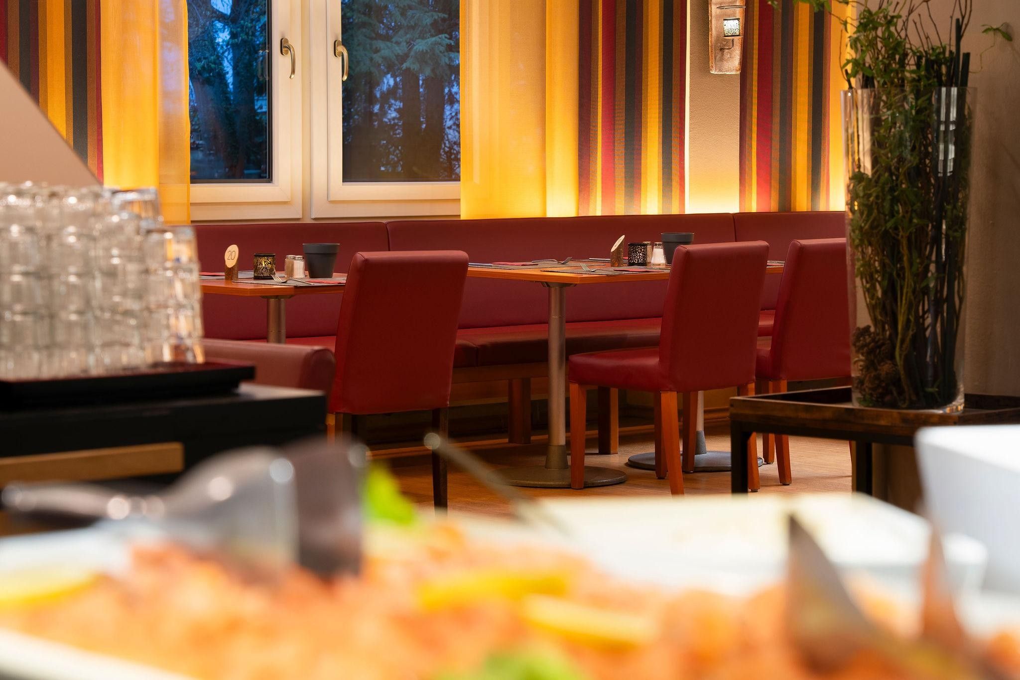 Interior de restaurant amb seients a cabines, taules i una finestra gran amb vista a arbres.