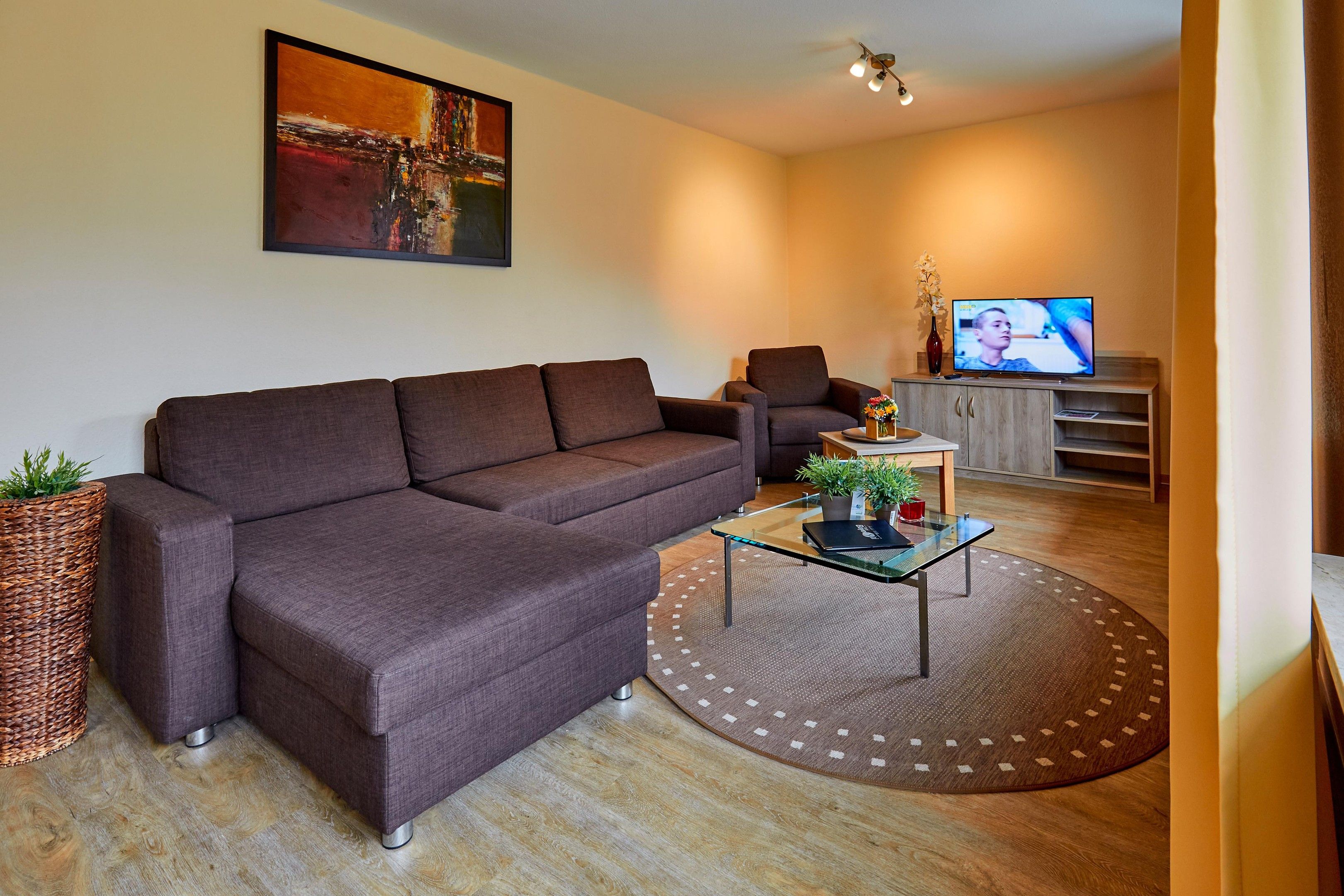 Una sala de estar moderna con un sofá modular, una mesa de centro de vidrio, un televisor y un jarrón decorativo.