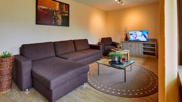 A modern living room with a sectional sofa, a glass coffee table, a television, and a decorative vase.