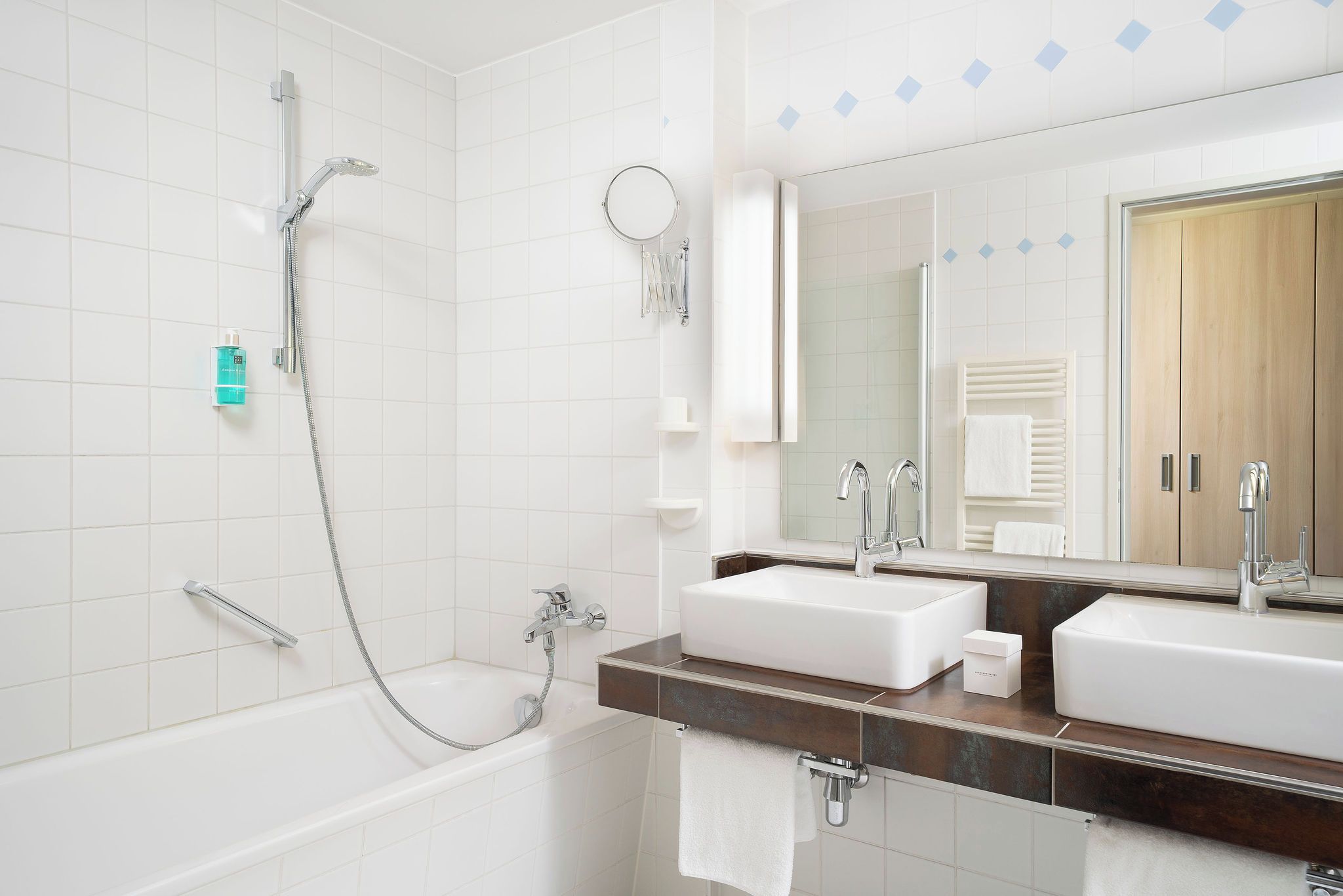 Een moderne badkamer met een badkuip, twee wastafels, een spiegel en een handdoekrek.