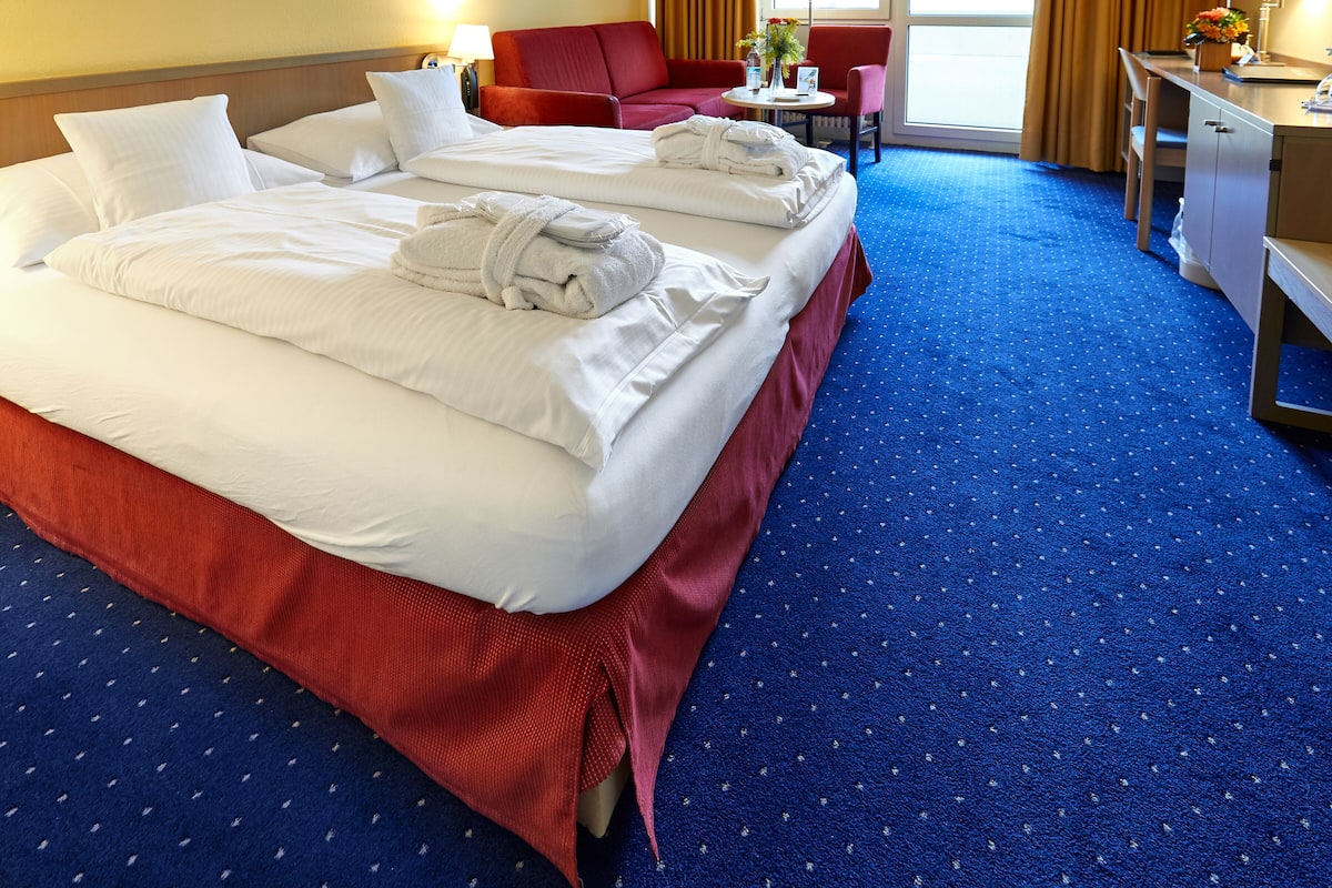 A hotel room with two beds, a red sofa, a desk with a lamp, and a TV.