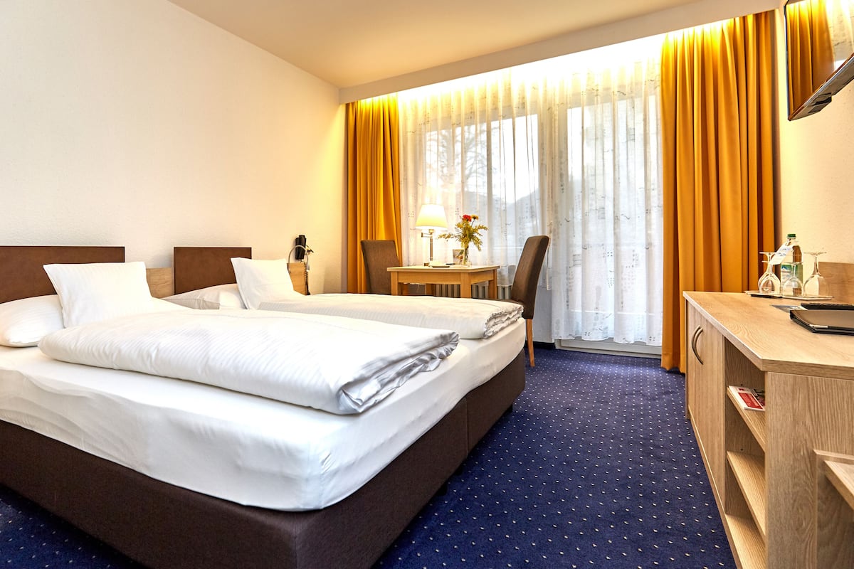 A hotel room with two beds, a desk, a chair, a lamp, and a window with curtains.