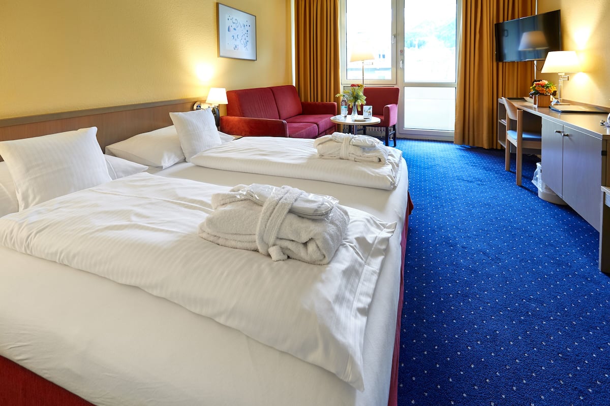A hotel room with two beds, a desk, a chair, a TV, and a window with curtains.