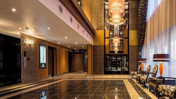 A spacious lobby with a high ceiling, a large chandelier, and a seating area with patterned chairs. - APA Hotel Okayama Ekimae (Okayama)