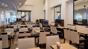 A modern restaurant interior with white brick walls, black and white chairs, and wooden tables. - APA Hotel Okayama Ekimae (Okayama)