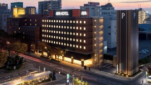 A modern hotel with a prominent APA sign, surrounded by other buildings and a parking area. - APA Hotel Okayama Ekimae (Okayama)