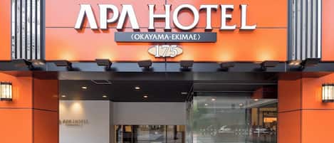 Exterior del hotel APA, con una fachada naranja llamativa, una entrada despejada y un letrero con la dirección bien visible.