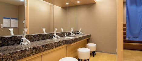 A modern bathroom with a marble countertop, multiple sinks, and white stools.