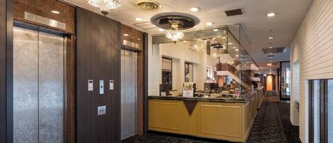 A hotel lobby with a central reception desk, elevators, and a patterned carpet.