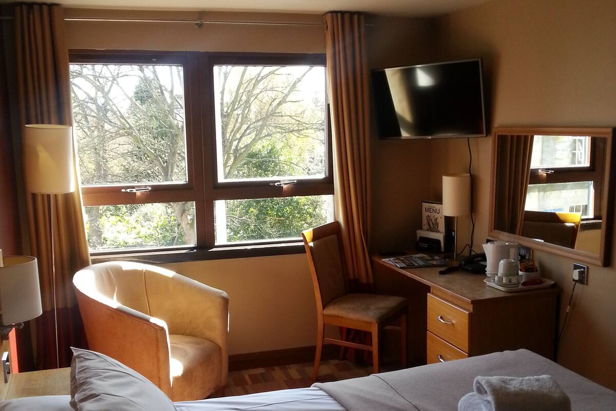 Ein Hotelzimmer mit Bett, Schreibtisch, Stuhl, Fernseher und einem Fenster mit Vorhängen.