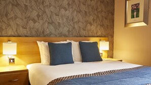 A neatly made bed with a blue blanket and pillows, two bedside lamps, and a patterned wallpaper. - Greyfriars Inn by Greene King Inns (St. Andrews)