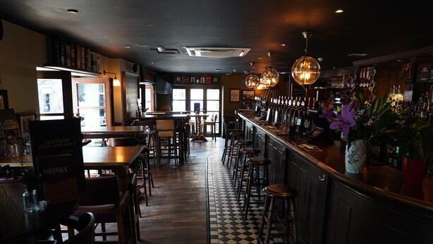 A bar area with a checkered floor, wooden bar stools, and a variety of bottles on the shelves. - Greyfriars Inn by Greene King Inns (St. Andrews)