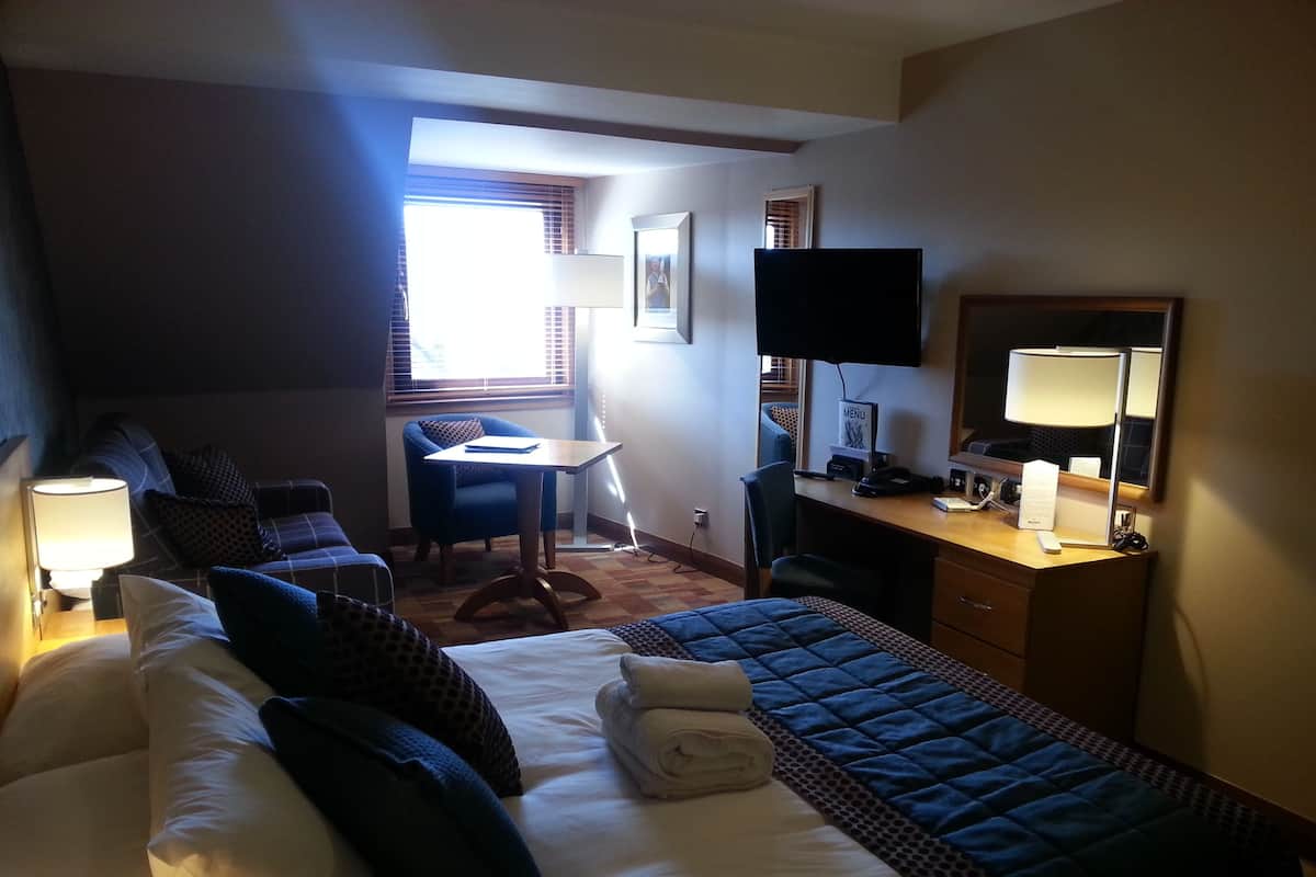 Ein Hotelzimmer mit Bett, Schreibtisch, Stuhl, Fernseher und Fenster.