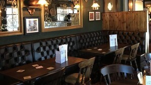 A restaurant interior with dark green walls, wooden paneling, and leather booths. Tables are set with menus and place cards. - Greyfriars Inn by Greene King Inns (St. Andrews)