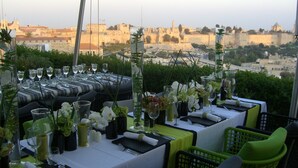 A rooftop dining area with tables set for a meal, overlooking a historic cityscape.