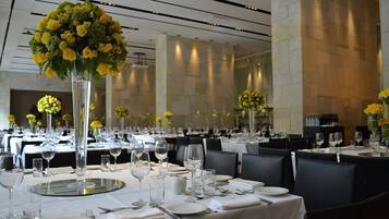 A formal dining area with tables set for service, featuring tall floral centerpieces and a modern interior design.