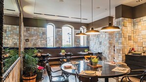 A restaurant with a modern interior, featuring a mix of wooden and tiled walls, multiple seating areas, and pendant lighting.