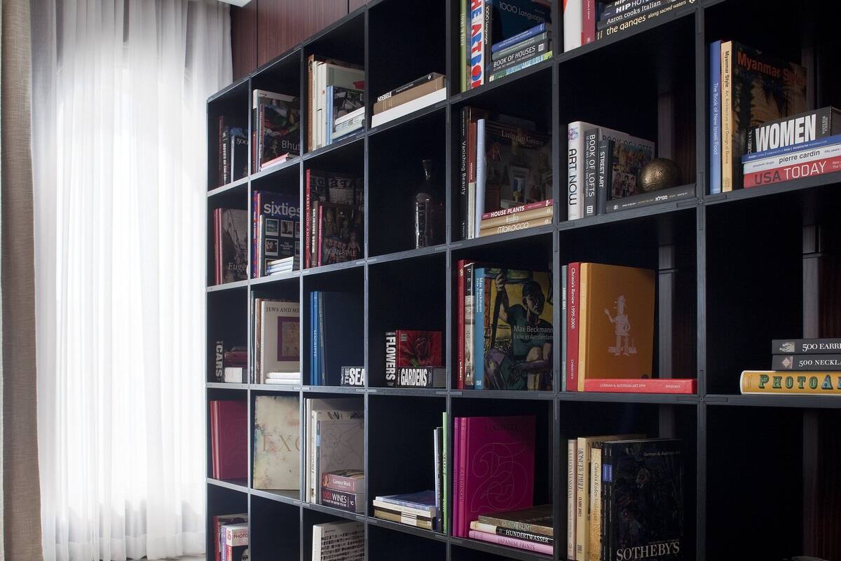 Une pièce avec une grande bibliothèque remplie de livres, une table en bois avec des magazines et une fenêtre avec des rideaux.