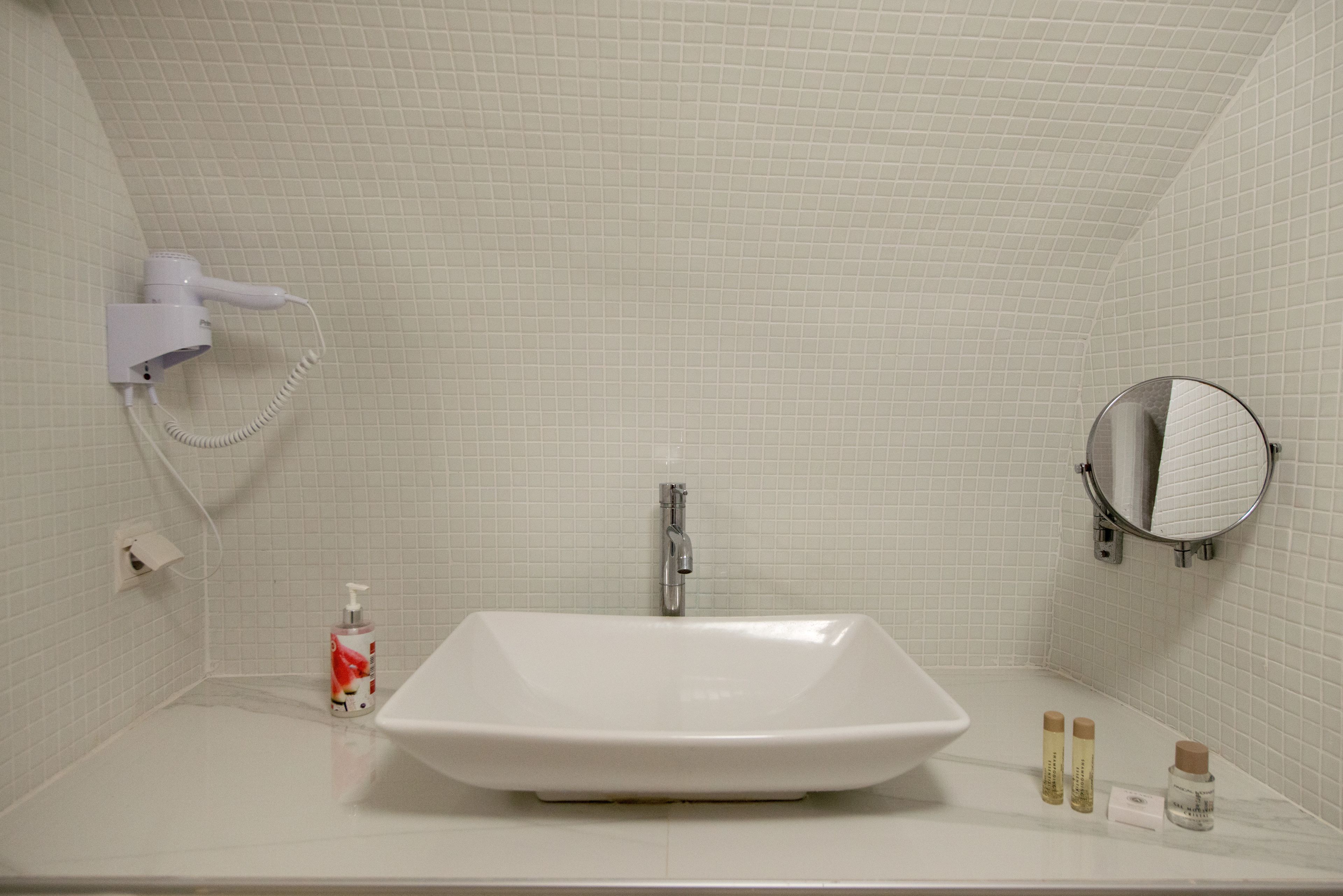 A bathroom with a white sink, a handheld showerhead, a mirror, and toiletries on the counter.