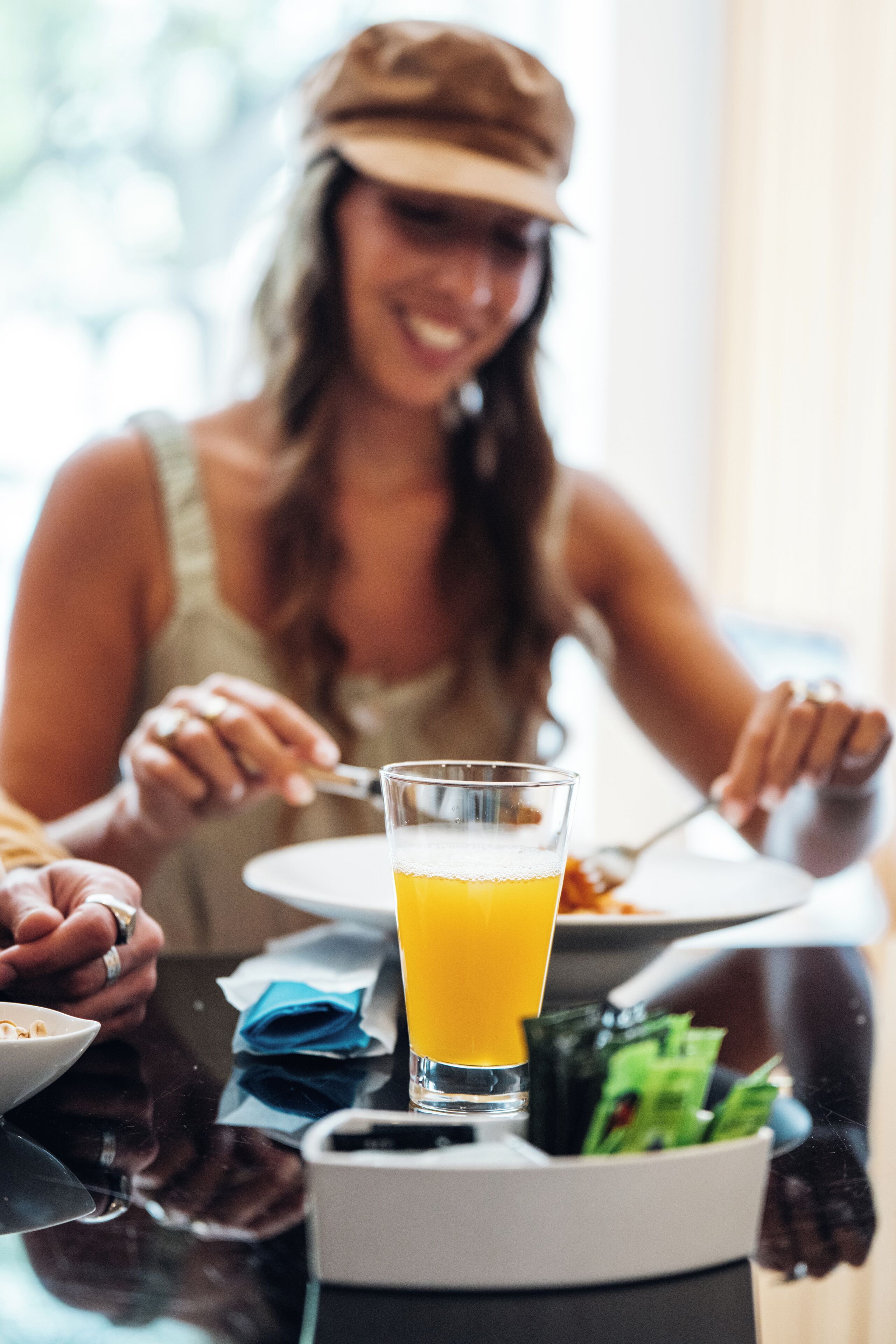 Una mesa de comedor con un vaso de zumo de naranja, un plato de comida y una servilleta.