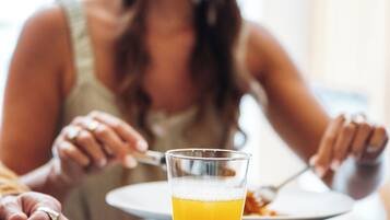 Una mesa de comedor con un vaso de zumo de naranja, un plato de comida y una servilleta.