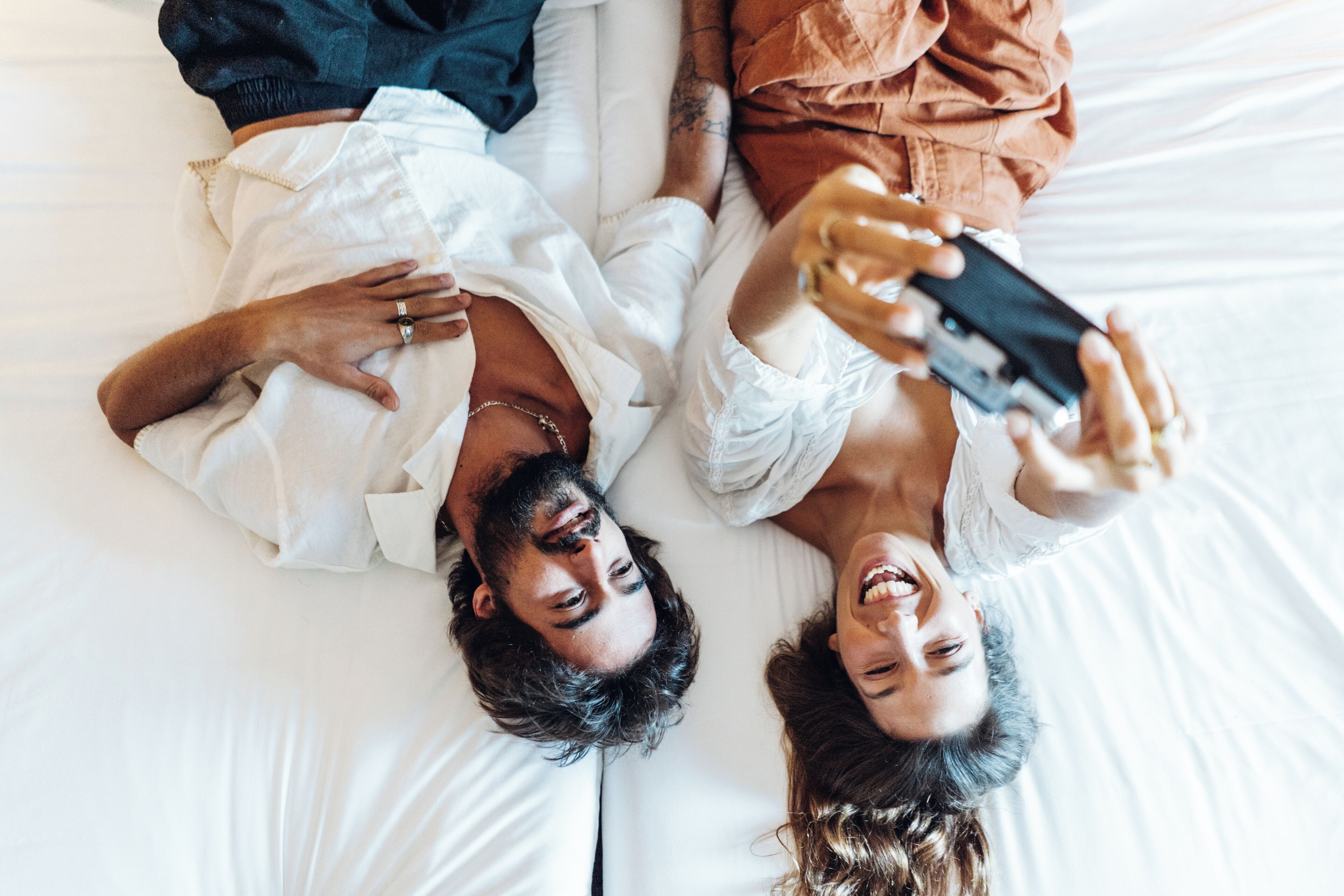 Dos personas recostadas en una cama, una sosteniendo un teléfono inteligente.