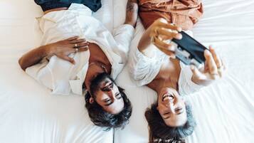 Dos personas recostadas en una cama, una sosteniendo un teléfono inteligente.