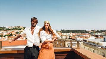 Una pareja parada en un balcón de madera con vista a un paisaje urbano.