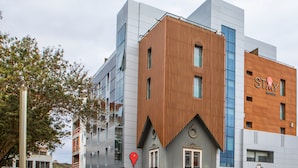 Un hotel moderno con una combinación de fachadas de madera y vidrio, un llamativo letrero con la palabra 'STAY' y un marcador de ubicación rojo en la fachada.