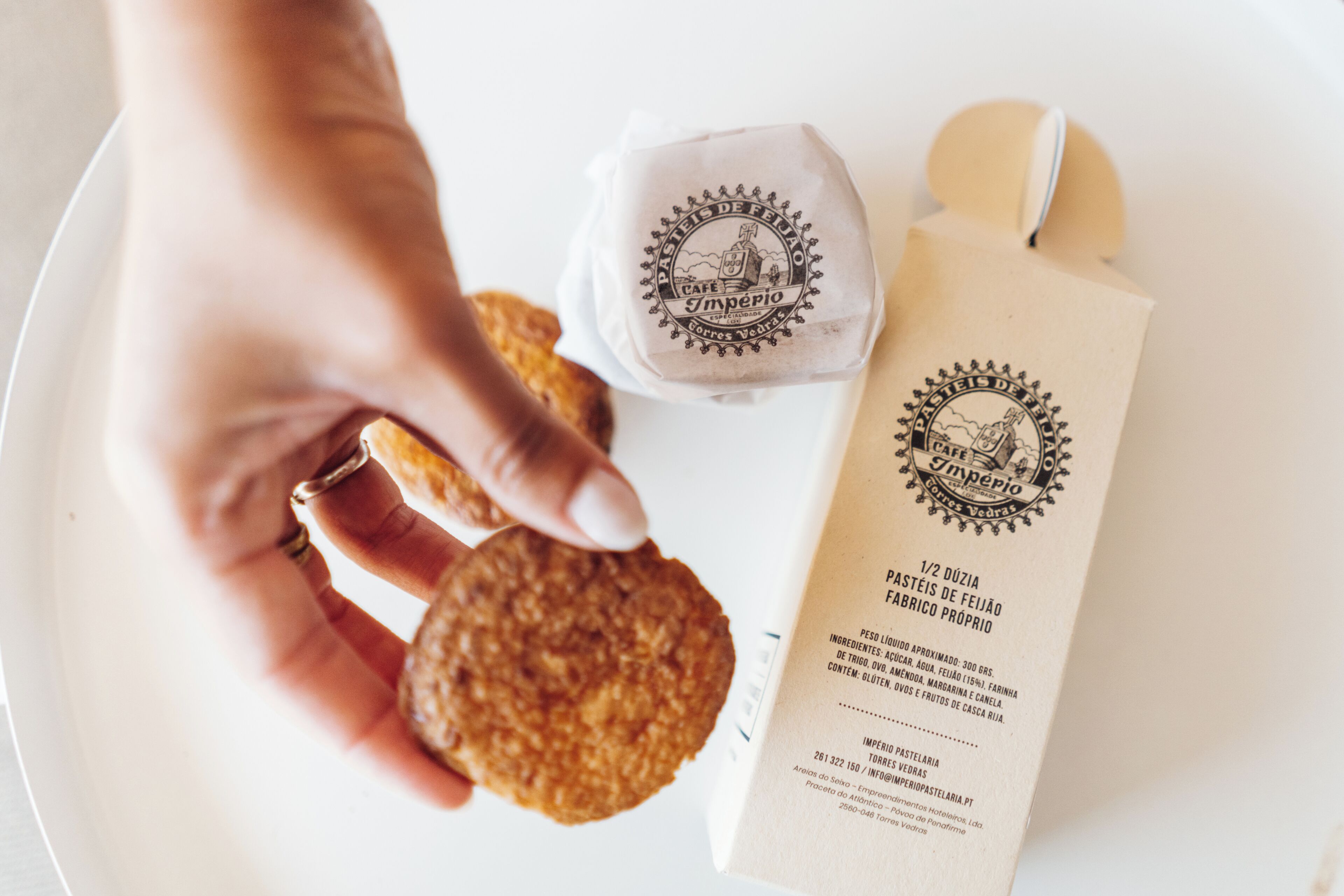 A hand holding a cookie next to a package labeled "Cafe Imperio."