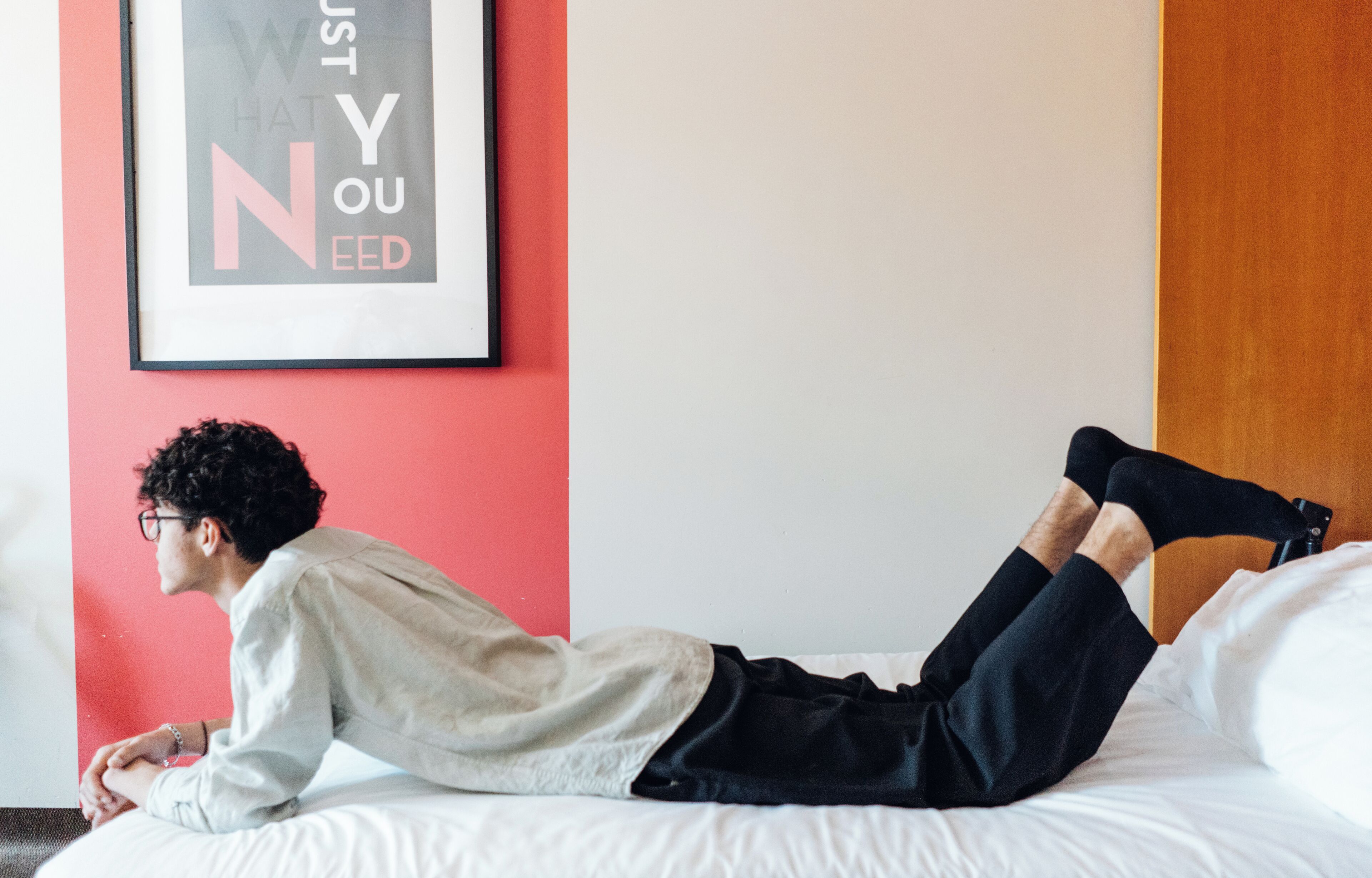 A person lying on a bed in a room with a red wall and a framed poster.