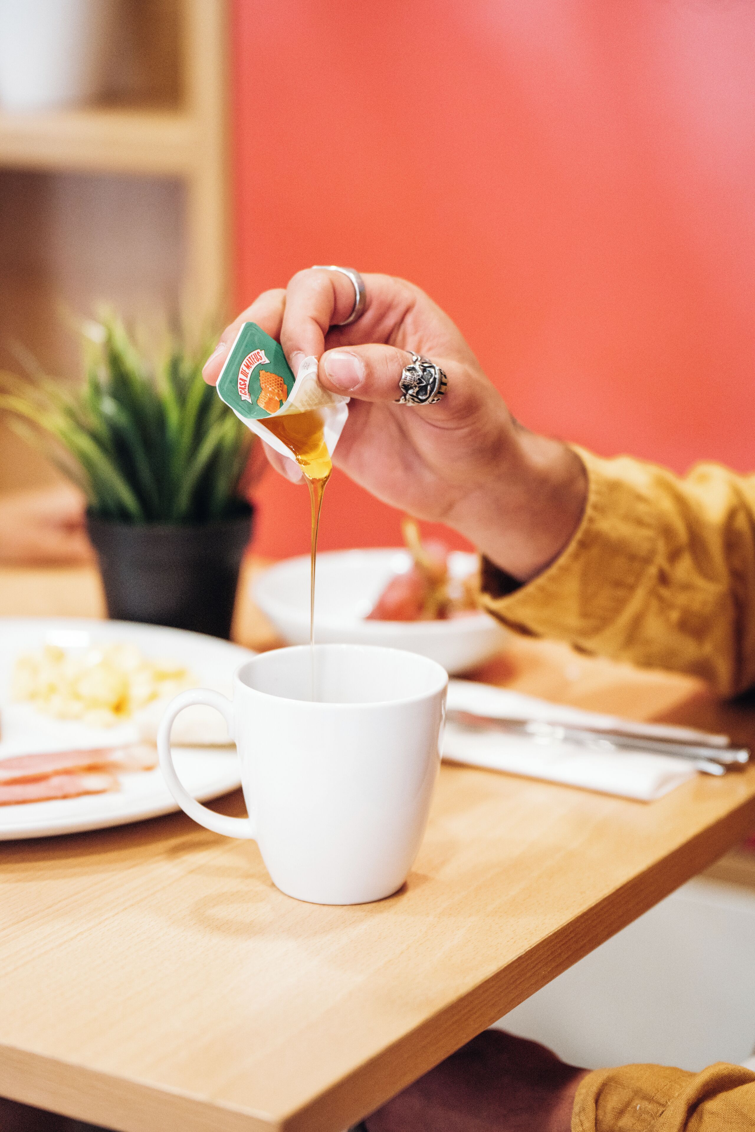 A hand pouring honey into a white mug on a wooden table.