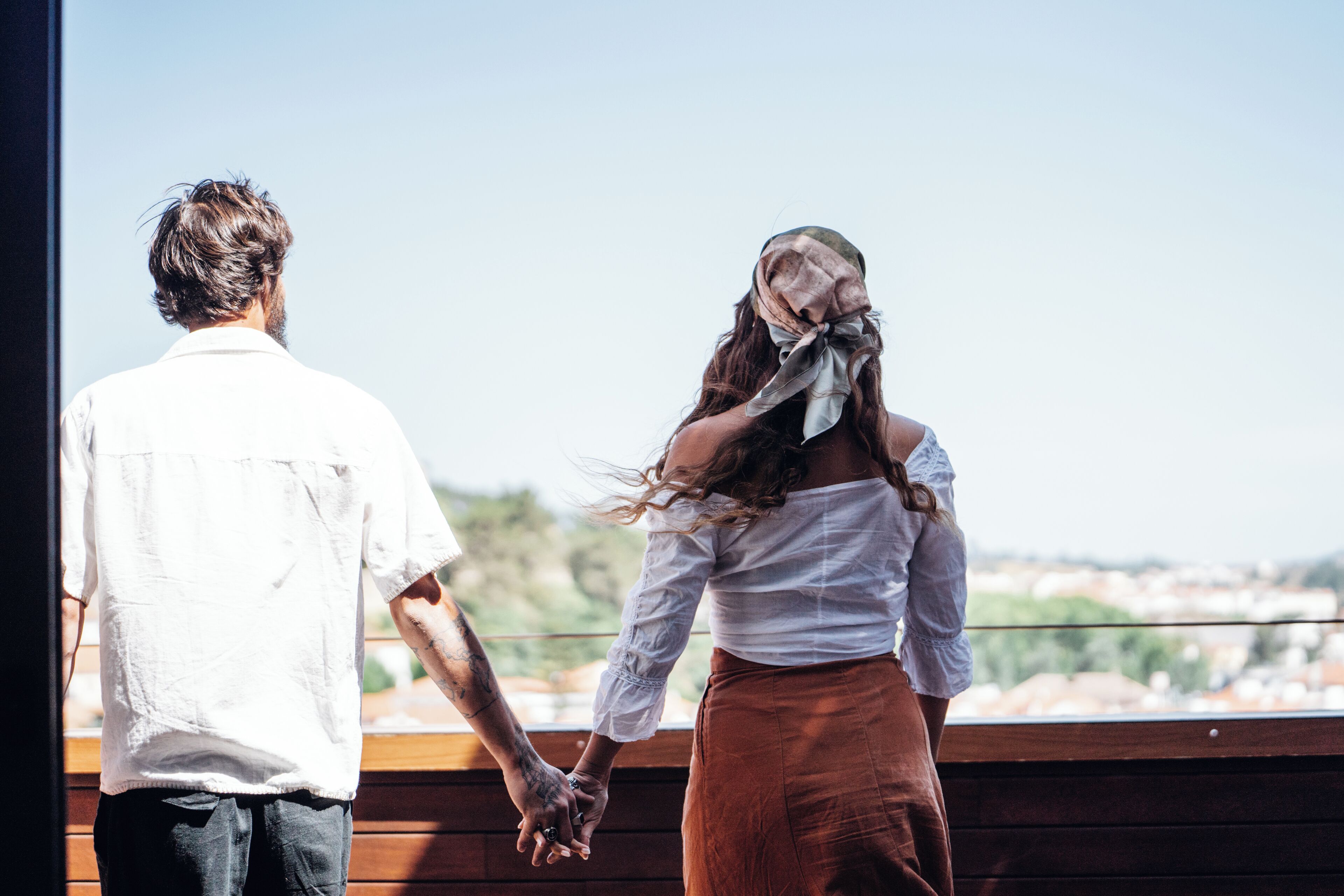 Una pareja tomándose de las manos en un balcón con vistas a la ciudad.