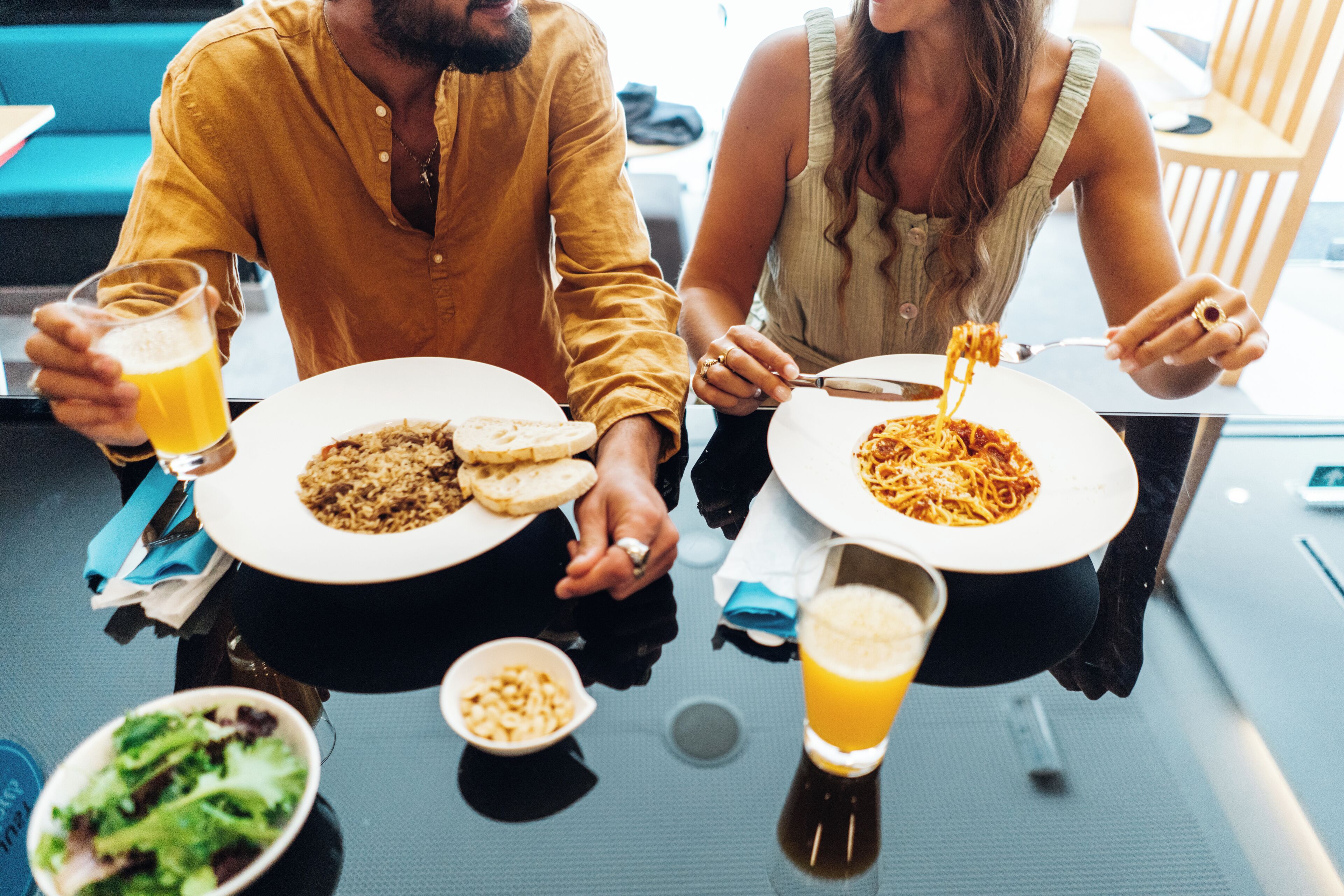 Una mesa de comedor con platos de comida, vasos de cerveza y un bol de ensalada.