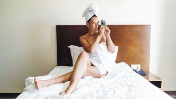 Una persona sentada en una cama dentro de una habitación de hotel, sosteniendo una cámara.