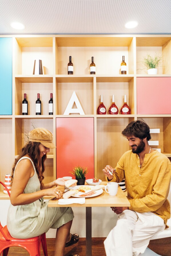 Un comedor con una mesa dispuesta para dos personas, rodeado de estanterías de madera con botellas de vino y una planta en maceta.