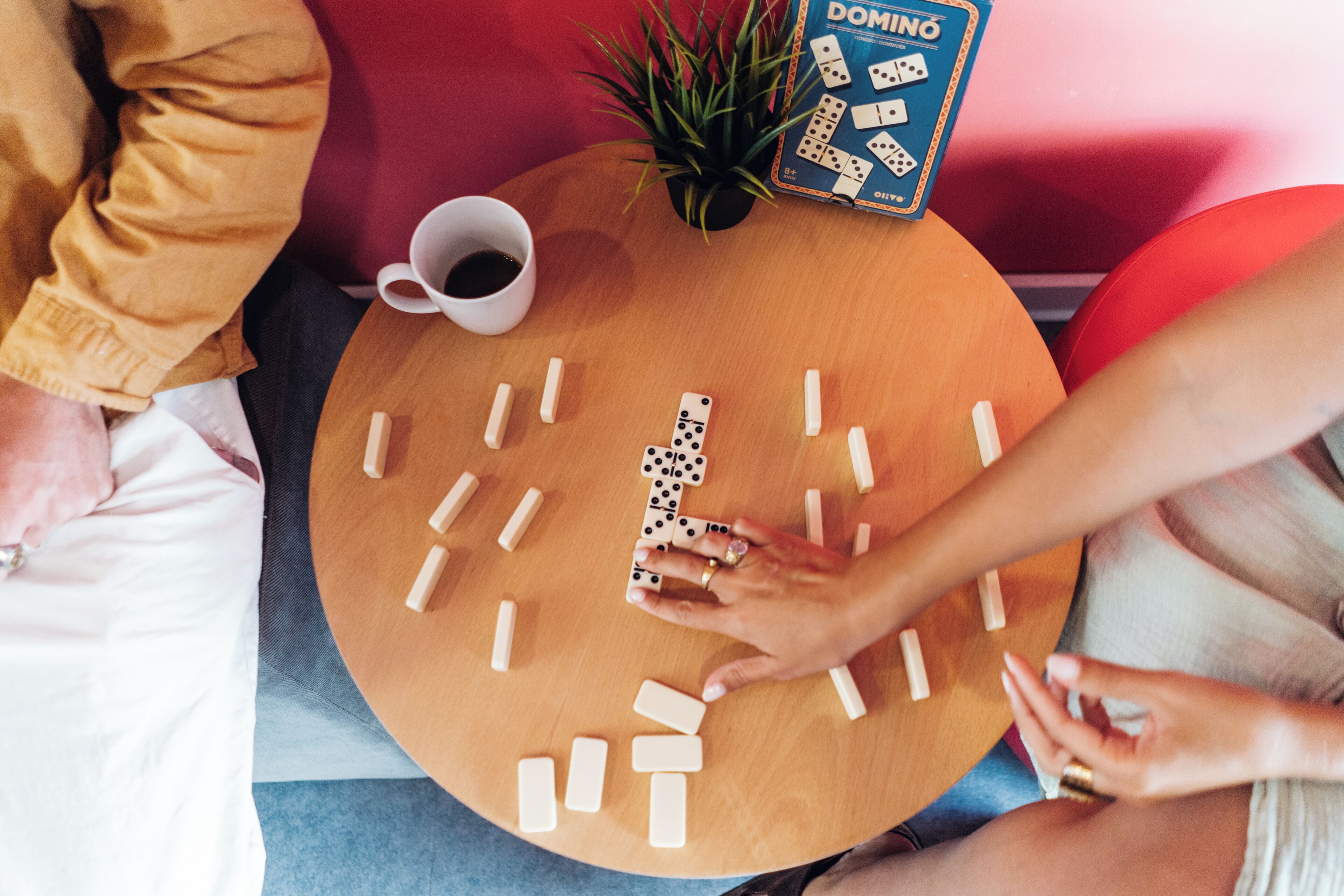 A round wooden table with dominoes, a cup of coffee, and a domino game box.