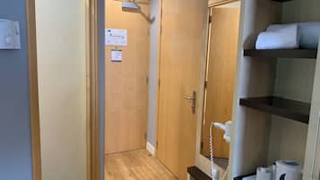 Habitación de hotel con puerta de madera, pared blanca, suelo de madera, repisa con artículos de aseo y teléfono fijo en la pared.