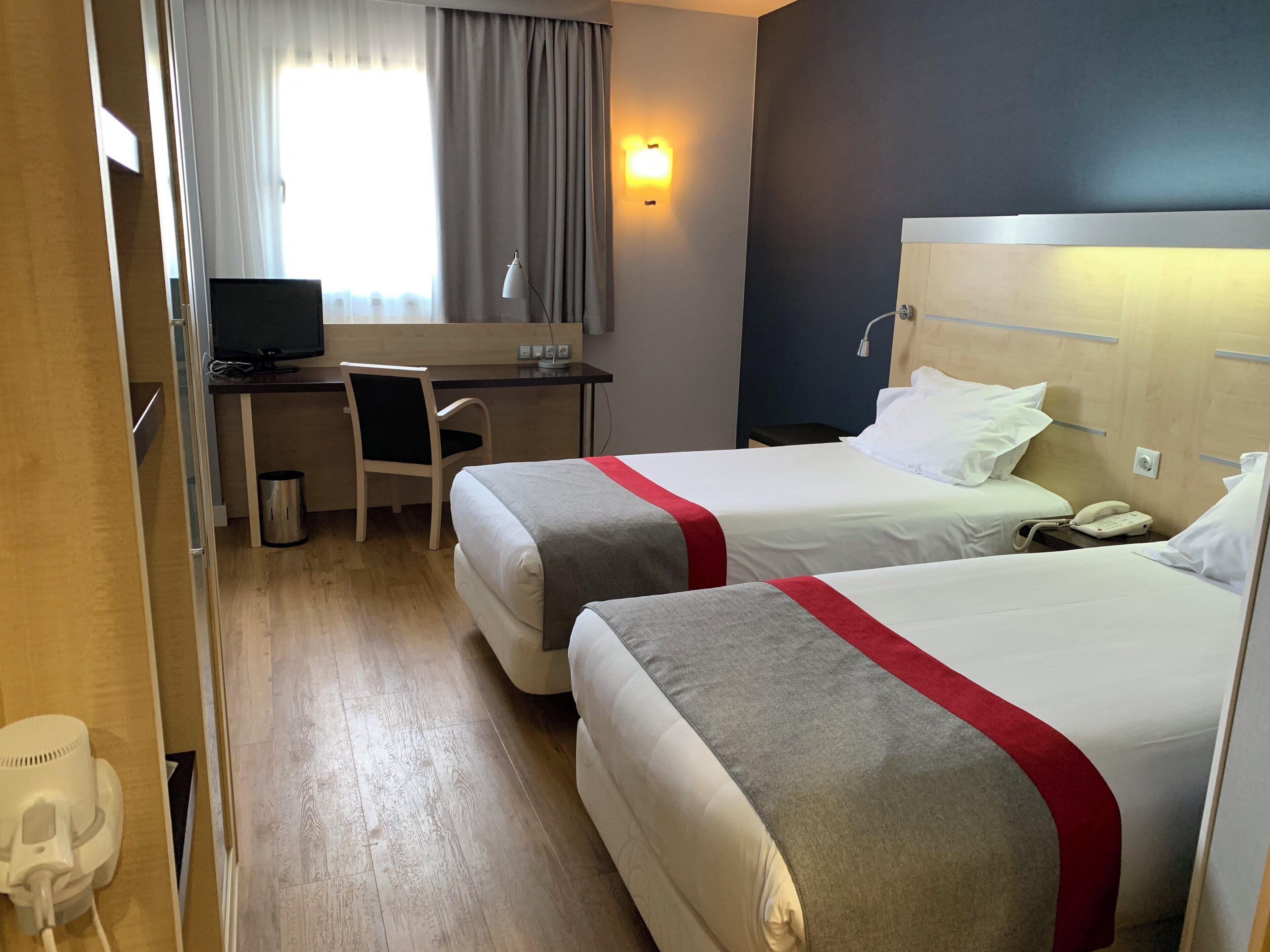A hotel room with two beds, a desk, a chair, a computer, and a telephone.